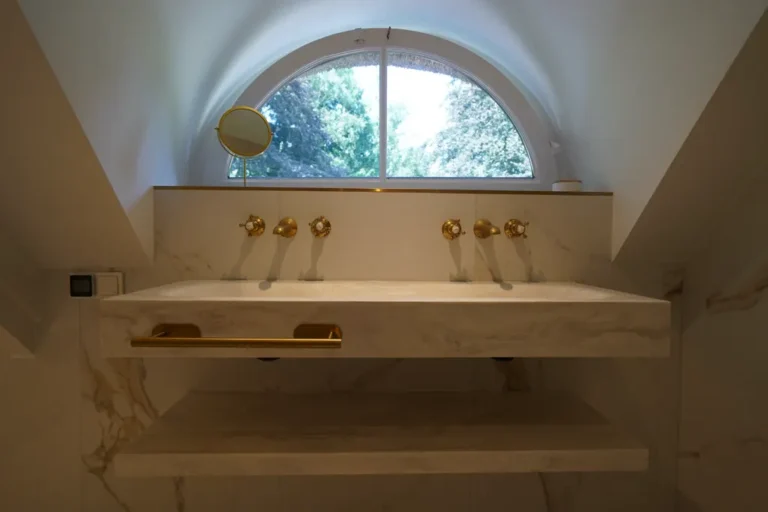 Marble vanity with gold taps beneath an arched window