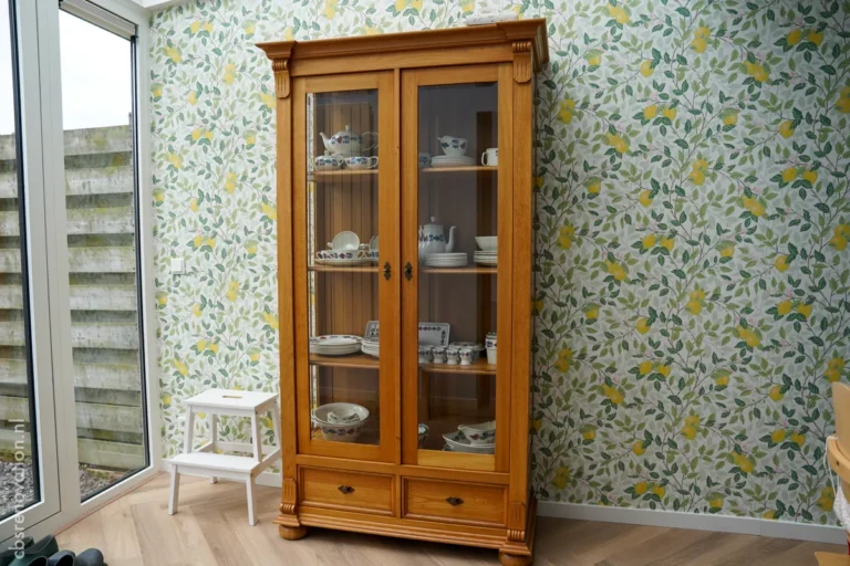 Oak display cabinet with china against lemon-print wallpaper