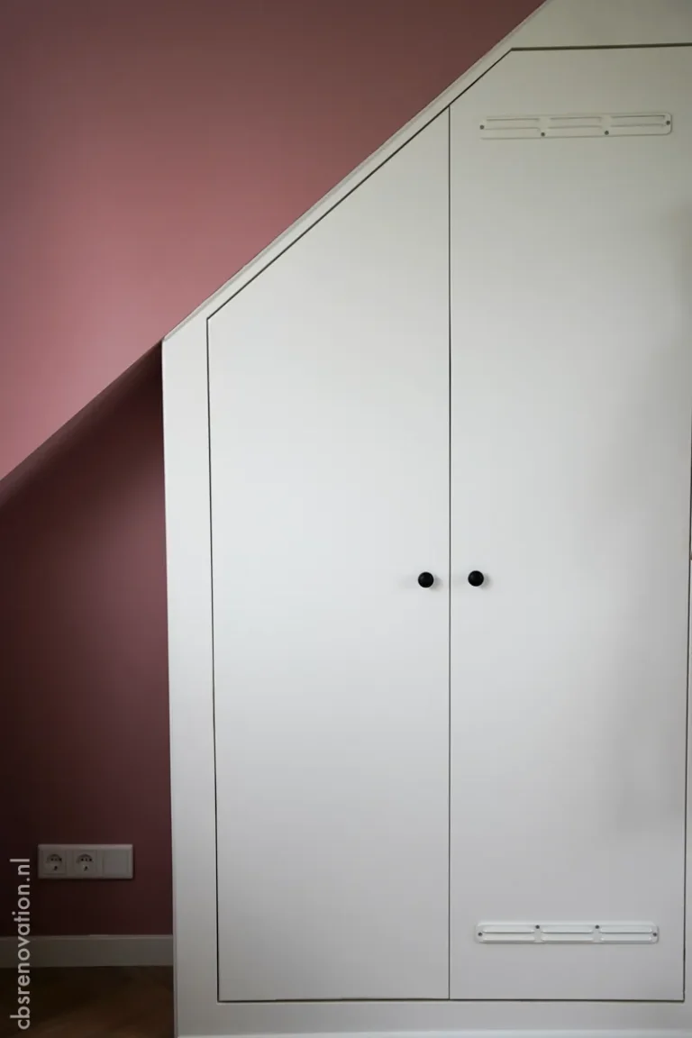 Fitted white wardrobe in an attic room with a pink wall