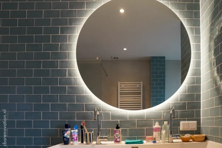 Bathroom vanity with a round illuminated mirror and blue tiles