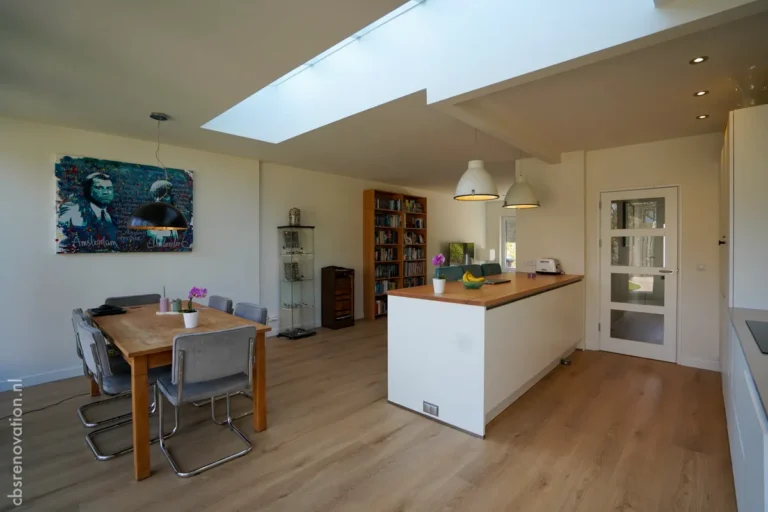 Bright open kitchen area with modern furniture, skylight, and wooden dining table, showcasing recent house renovation.