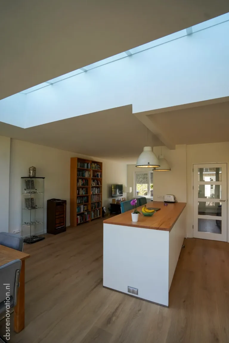 Bright open space featuring a kitchen island with wooden countertop, bookshelves, and natural light from skylights.