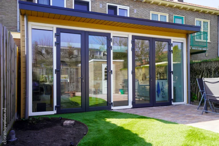 Modern glass doors open to a renovated patio with lush green grass and brick paving, showcasing the transformation of the house.