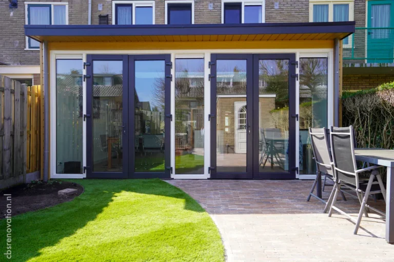 Modern glass doors open to a renovated outdoor space, featuring a lawn and patio furniture, showcasing a house renovation.