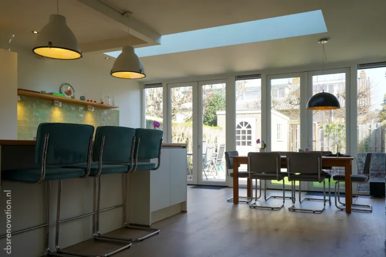 Renovated open-concept kitchen with bar seating, modern lighting, and large windows overlooking a garden.