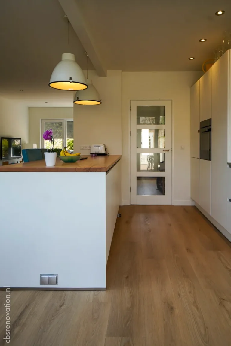 Modern kitchen with light wood flooring, white cabinetry, and pendant lights, showcasing a newly renovated space.