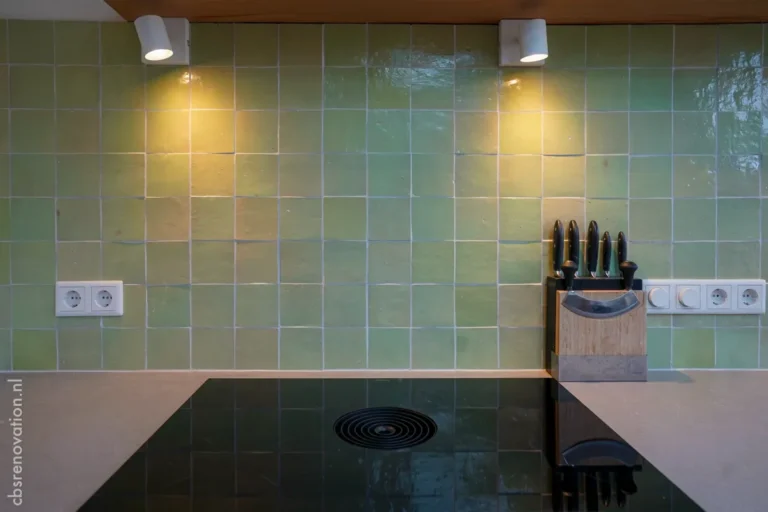 Green tiled backsplash in a kitchen with modern lighting, a black cooktop, and a knife block on the countertop.