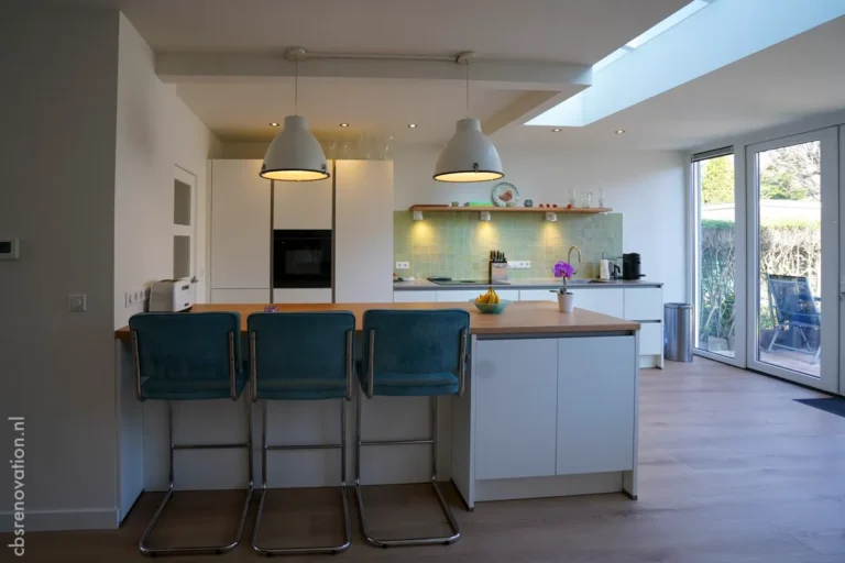 Modern kitchen renovation featuring sleek white cabinetry, a wooden bar counter, and stylish pendant lights.