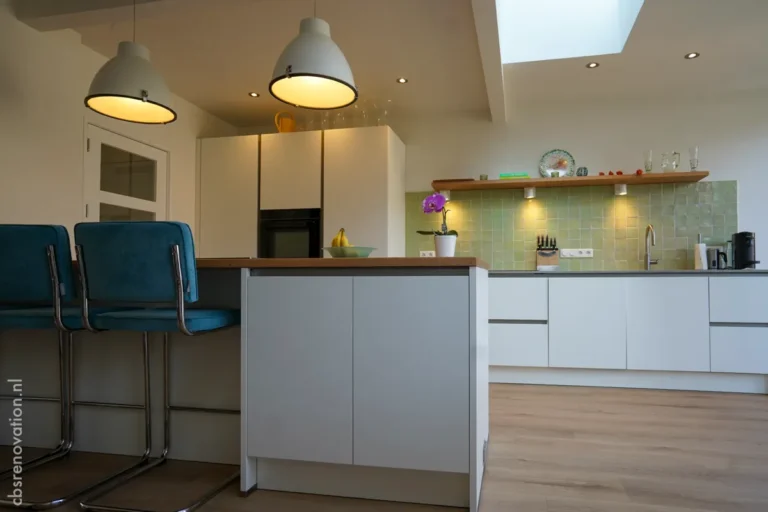 Modern kitchen renovation featuring a wooden island, sleek cabinetry, green tiles, and stylish pendant lights.