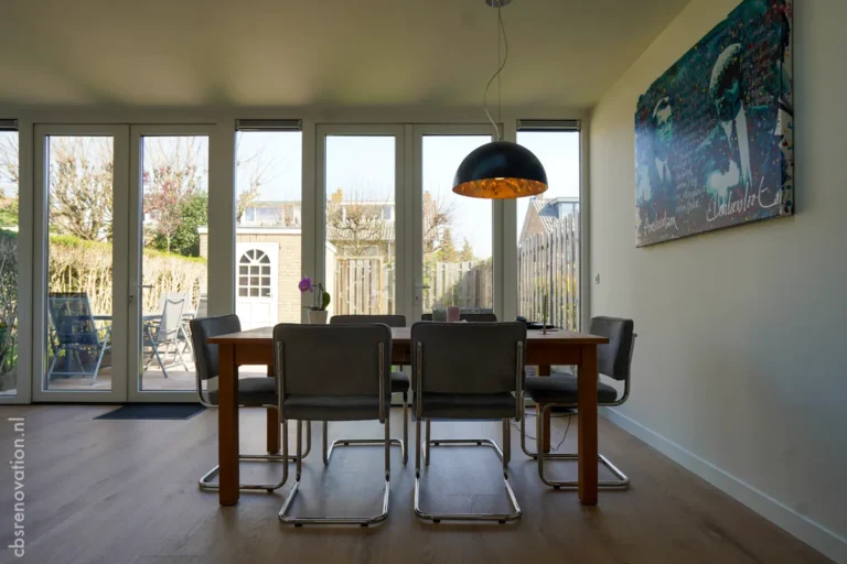 Bright dining area featuring a wooden table, modern chairs, and large windows overlooking a garden, showcasing recent renovations.