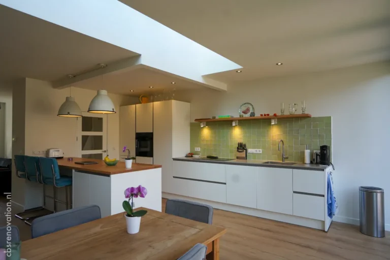 Modern kitchen featuring white cabinetry, green tiled backsplash, wooden counter, and open space with natural light.
