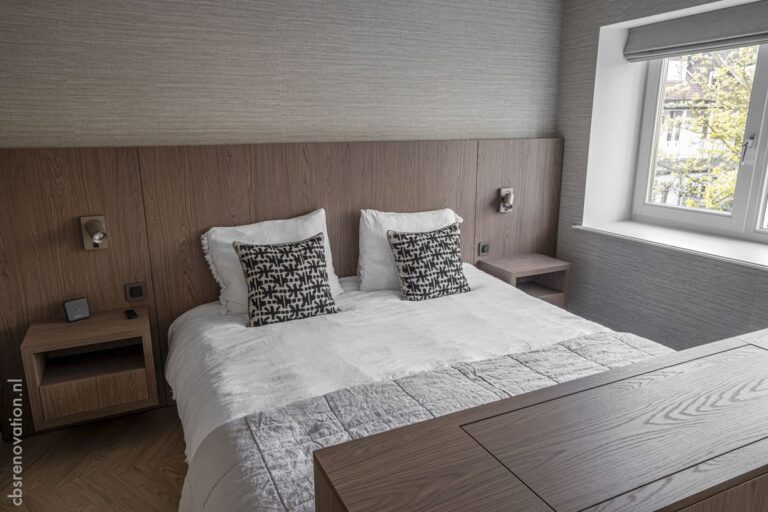 Bedroom with a wood-panelled headboard, bedside tables and a window onto the street