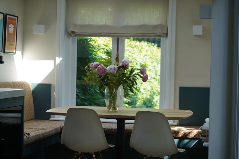 Dining table and chairs beneath a window with a linen roman blind